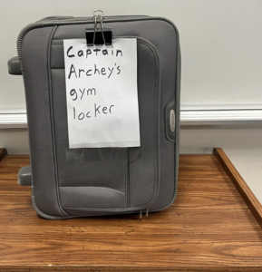 Suitcase labeled "Captain Archey's gym locker"