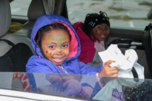Two children with face-paint on hold bags of candy in the back of a car.