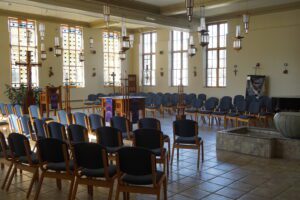 A photo of the inside of the St. Ignatius Chapel, with chairs, a cross, lights, pupil and light shining through the windows.