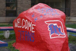 A red-painted rock outdoors on the McNichols Campus featuring the words, WELCOME TITANS and SOAR 2024.