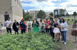 An image of several people standing behind a garden with produce in their hands.