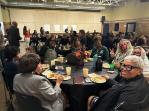 A potograph of several individuals sitting at tables sharing a meal together