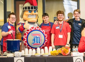 Image of four students and Tommy Titan in front of table at chili cookoff