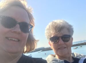 Selfie image of two women with water and boats in the background