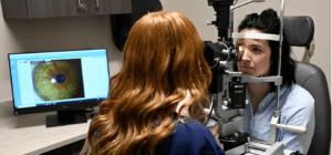 An image of two individuals, one is an optometrist and the other a patient sitting in a chair having her eyes examined.