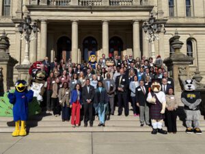 Mascots, students and members of higher education institutions stand on the capitol steps in Lansing.