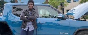 Agholor leans against a blue Rivian electric vehicle, outdoors.
