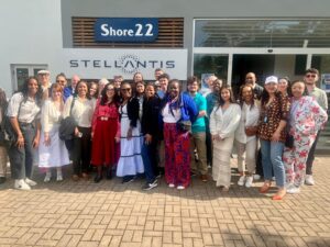 A group of more than 20 people standing outside a building under a Stellantis sign.