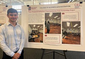 Mark Formosa poses in front of a poster presentation entitled Titan Financial Initiative
