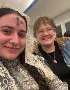 Two people smile for a photo indoors, one wearing a cross from ashes on her forehead.