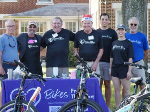 Seven people stand and pose for a photo outdoors with bicycles in front of them.