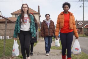 Three students walking down the street carrying Meijer bags of food