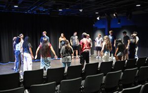 An image of several students standing in a circle on stage at UDM's Blackbox Theatre