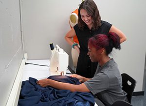 Two students working with fabric at a sewing machine.