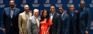 Eight people stand in front of a blue University of Detroit Mercy backdrop