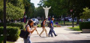 A photo of students walking in front of the Jesus statue outdoors on the McNichols Campus.