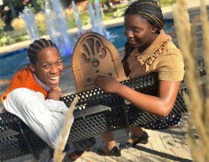 Two students sit on a bench near the Fisher Fountain, one holding an old radio.