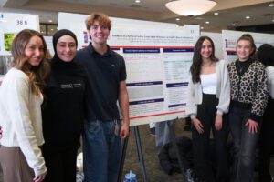 Five students stand next to their research board inside of the ballroom of the Student Union.