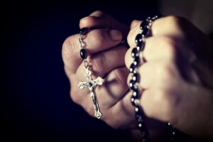 Two hands holding a rosary in prayer