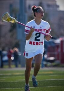 An image of a female on the lacrosse playing field wearing a Detroit Mercy lacrosse jersey with the number 2 on the front and holding a lacrosse stick.