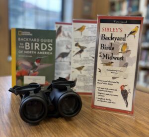 Birdwatching books and binoculars sit on a table inside of the McNichols Campus Library.