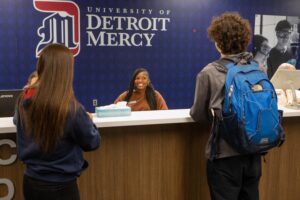 Three people talk at the front desk inside of the Office of Admissions at University of Detroit Mercy.