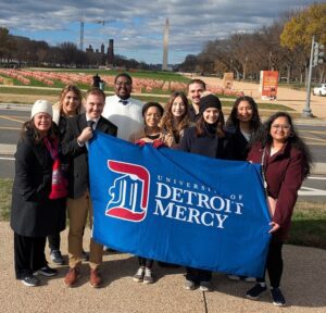 Group of people holding Detroit Mercy flag standing in front of Washington Memorial