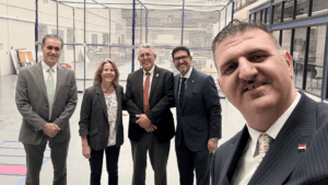 Five people stand and pose for a photo inside of the Engineering Building's High Bay at UDM