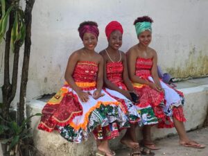 Three Brazilian women in colorful dresses sitting on a bench