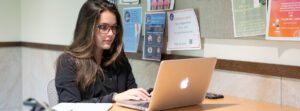 A student studies with a laptop and other materials in front of her inside of a lobby at the College of Health Professions Facility.