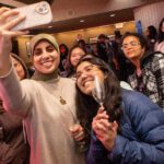 A student takes a selfie of herself and six of her friends, with others in the background inside of the Titan Club.